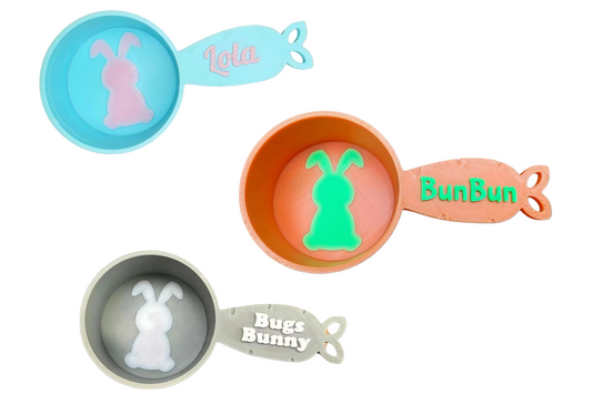Three personalized and colorful measuring cups with bunny designs and names on a white background
